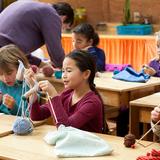 Davis Waldorf School Photo #8 - In addition to our rigorous academic program, we have a robust "subject" program that seeks to fulfill our mission of educating the whole child. Here second grade students learn to knit in a handwork class. Additionally, our students have Spanish, games and movement, gardening, art, woodworking, music, and more.