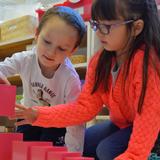 The Gladwyne Montessori School Photo #1 - 3rd year primary student gives a lesson to a 2nd year primary student using the iconic pink tower, specifically designed for children to learn about space, size, and comparison in a concrete manner.