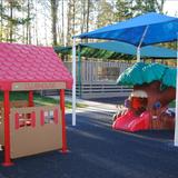 Stonehenge KinderCare Photo #10 - Infant/Toddler Playground features an open climb through tree and a covered picnic clubhouse with table and benches. This playground also has a rubber play surface and a tricycle track.