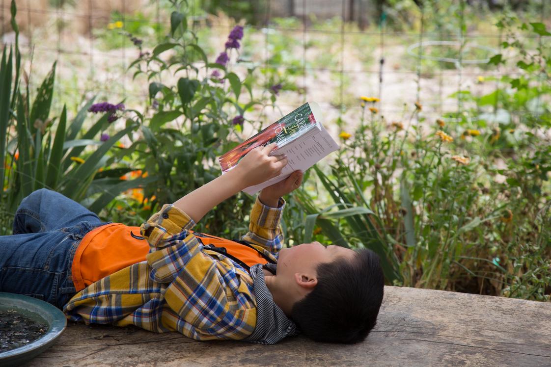Meher Schools Photo #1 - A student reads a book in our 3/4 acre organic 7-Circles Garden. Elementary students attend gardening class once a week and help compost, prepare soil, weed, plant, and harvest.