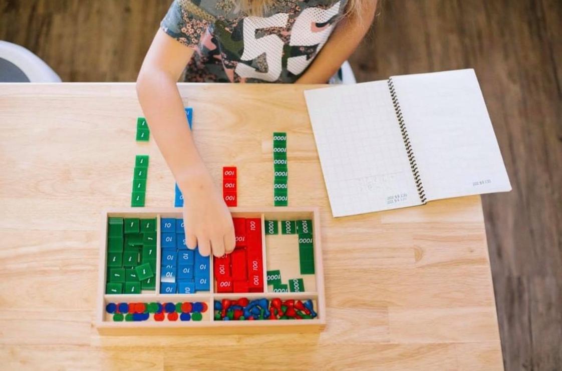 Guidepost Montessori School Photo #1 - The didactic materials in a Montessori classroom allow the child to experience the concepts being taught with both their hands and their mind. This is a child using the stamp game to perform mathematical equations. This tool shows the child the value making it concrete for the child to make sense of the quantity.